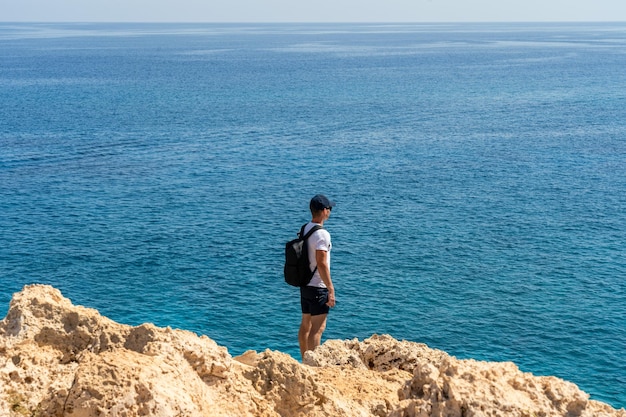 Man Traveler steht auf Felsen und blickt auf das blaue Meer Fernweh-Konzept