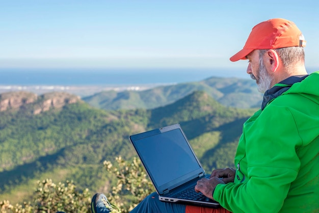 Man Wanderer mit einem Laptop, der auf der Spitze der Berge arbeitet Remote-Arbeit mit Laptop Man sitzt auf der Spitze