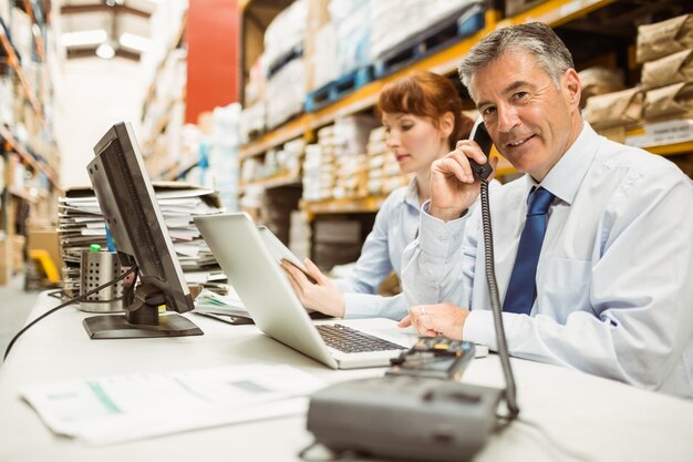 Foto manager, der an laptop arbeitet und am telefon am schreibtisch spricht