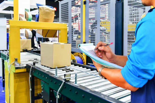 Manager Ingenieur, der Pappkartons auf Förderband im Distributionslager überprüft.