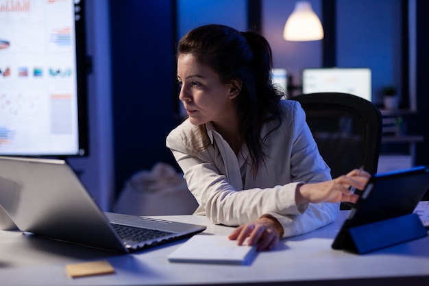 Managerin, die gleichzeitig Laptop und Tablet verwendet, um im Büro für Unternehmensgründungen an Finanzberichten zu arbeiten