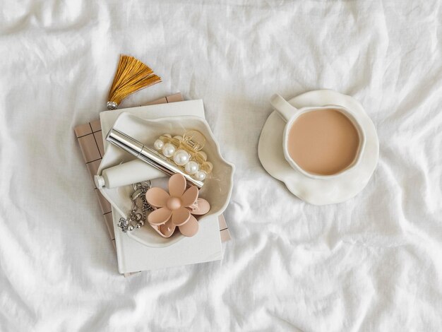 Una mañana acogedora en la cama una taza de té con leche un tazón de crema un clips de pelo máscara de pestañas cuadernos en sábanas blancas en la cama