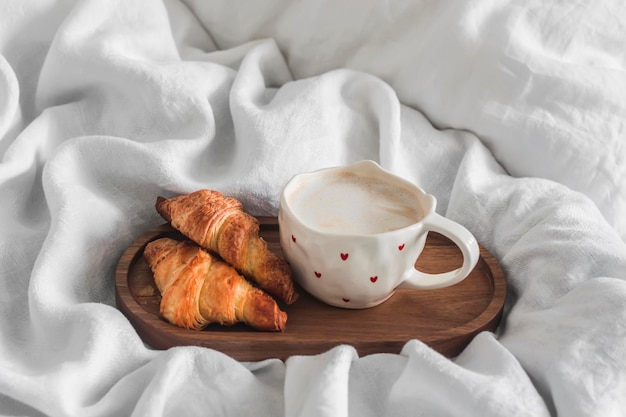 Foto una mañana acogedora desayuno en la cama taza de capuchino y croissants en una bandeja de madera en una cama con sábanas blancas