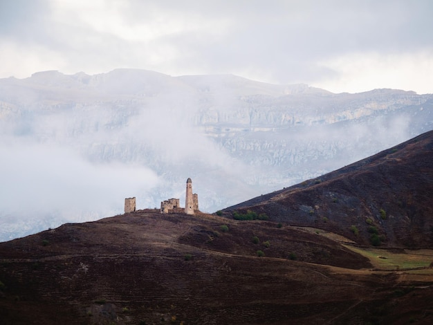 Mañana brumosa en las montañas del Cáucaso Torre medieval en el fondo de la ladera de la montaña brumosa Región de Ingushetia