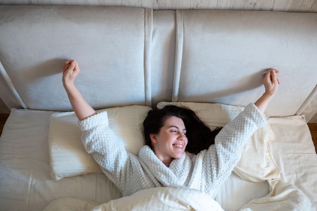 Mañana en la cama mujer despertando acostada en la cama con sábanas blancas