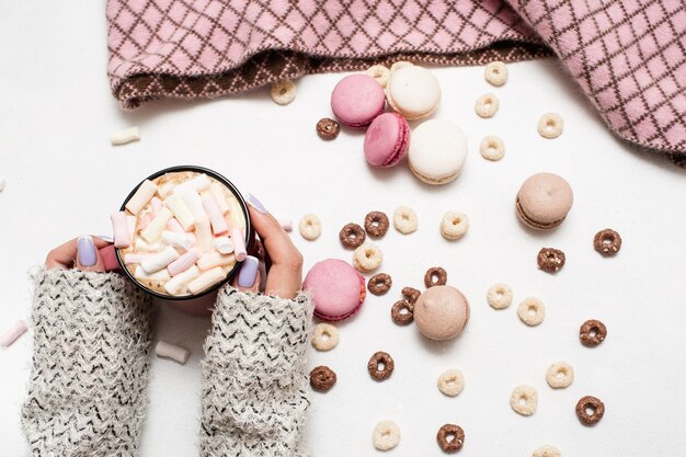 Mañana cómoda con café con leche y macarrones. Bebida caliente con malvavisco en manos de mujer, surtido de dulces coloridos