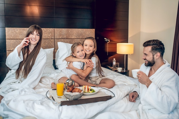 Foto mañana familiar. niños jugando mientras mod hablando por teléfono, papá tomando café