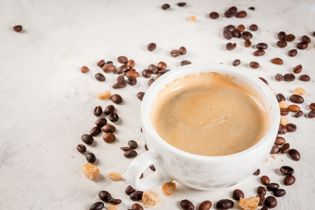 Mañana. Fondo de alimentos Granos de café, una taza de café recién hecho y una cuchara de azúcar moreno de caña sobre una mesa de piedra blanca. Copia espacio