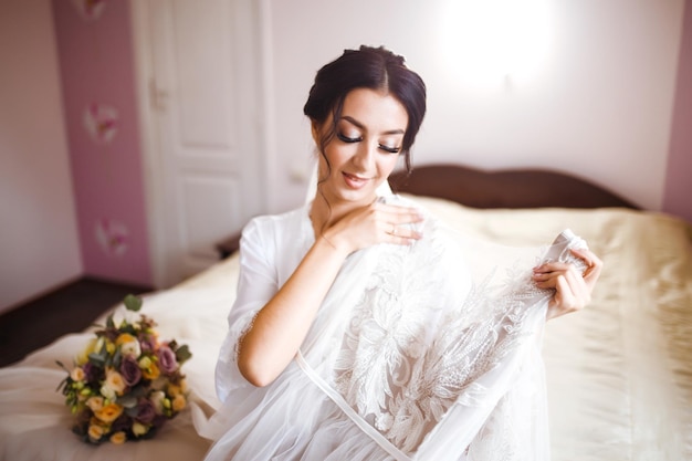 Mañana de hermosa novia cerca del vestido de novia La novia con una túnica blanca sostiene su vestido de novia.