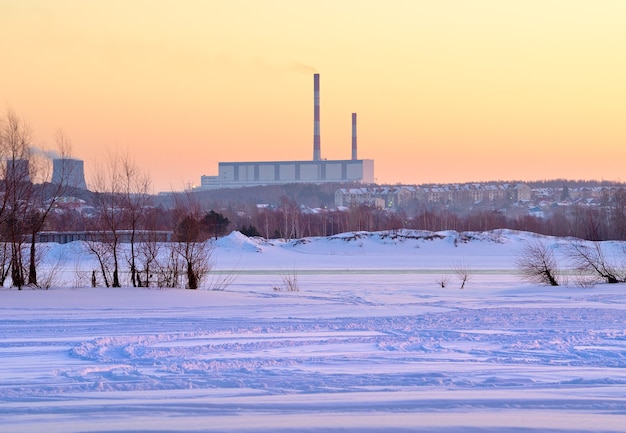 Mañana de invierno en la Ob. Orilla del río cubierto de nieve congelada, tuberías de la estación de calor en el horizonte en Novosibirsk