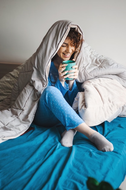 Mañana de una mujer rizada cubierta por la manta disfrutando de una bebida caliente