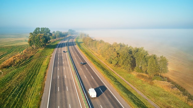 Mañana de niebla de otoño mágico soleado. Vista aérea de la carretera con coches. Carretera asfaltada cubierta de niebla. Temprano amanecer brumoso. Magistrado M1 en Bielorrusia