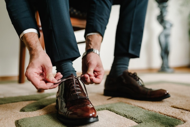 Foto la mañana del novio antes de la ceremonia de la boda usa zapatos el hombre de negocios ata los cordones de los zapatos profesiones de estilo masculino para prepararse para el trabajo para la reunión