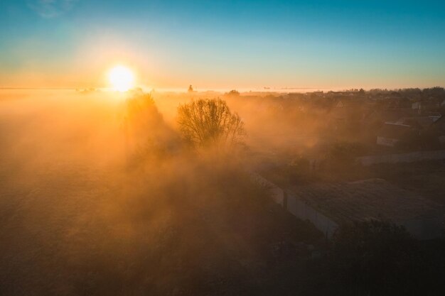 Mañana de otoño con niebla en el pueblo Siluetas de árboles y casas en la niebla