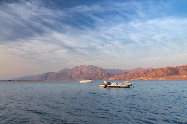 Mañana soleada en la orilla del mar con lancha y montaña en el fondo bajo las nubes de luz Dahab Egipto