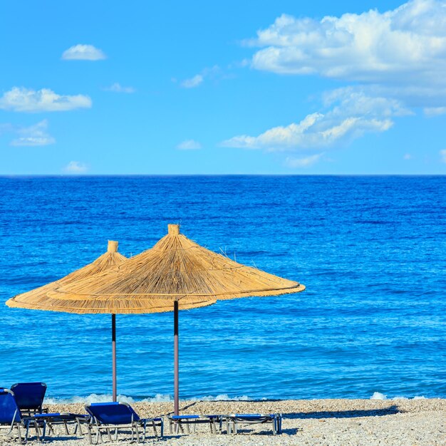 Mañana de verano playa de guijarros con hamacas y sombrillas de paja (Borsh, Albania). Cielo azul con algunas nubes.