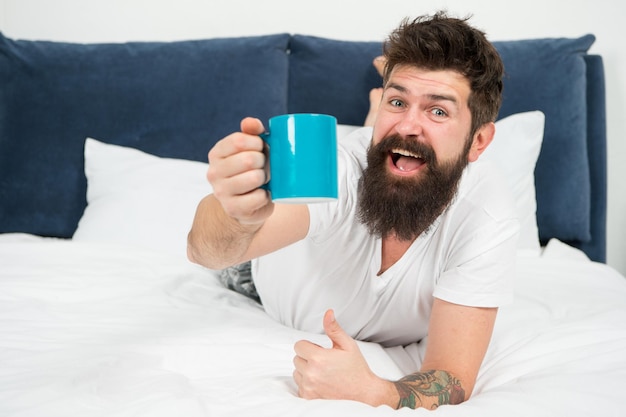 La mañana se vuelve mucho mejor con un buen café Relájese y descanse Lleno de energía El café afecta el cuerpo Hombre guapo hipster relajándose en la cama con una taza de café Hipster barbudo disfruta del café de la mañana