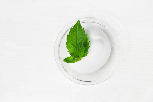 Una mancha de crema cosmética blanca sobre una mesa de madera blanca con hojas de menta verde