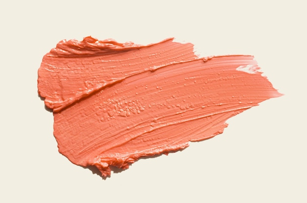 Mancha de lápiz labial de satén de color rosa naranja aislada sobre un fondo beige