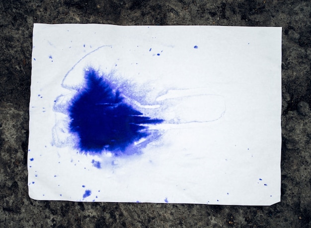 Mancha roxa de tinta uma folha de papel branco sobre uma superfície de pedra. Ponto colorido azul em papel branco com lugar vazio. Pano de fundo abstrato da base da base. Espaço para texto