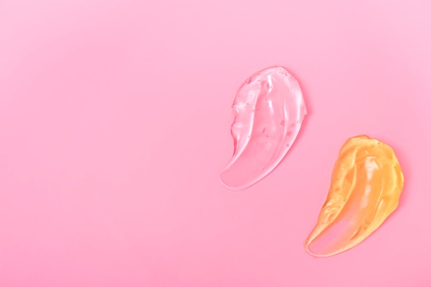 Manchas cosméticas em gel para cuidados com a pele em um creme de fundo rosa, loção de leite descascada, gotas de textura Fechar com espaço de cópia