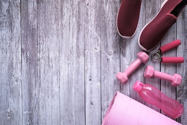 Mancuerna de color rosa, zapato y botella sobre fondo de madera