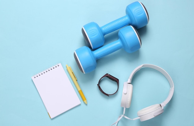 Mancuernas y auriculares portátiles y pulsera inteligente sobre un fondo azul Plan de entrenamiento Accesorios de fitness Vista superior