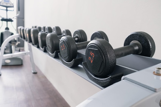 Mancuernas de metal negro de diferentes pesos en un estante en un gimnasio