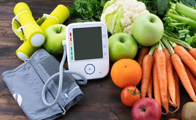 Foto mancuernas de monitor de presión arterial y frutas frescas con verduras contra la mesa de madera estilo de vida saludable y prevención del concepto de hipertensión