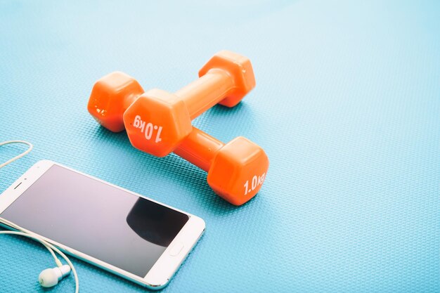 Mancuernas y teléfono inteligente en una estera de yoga