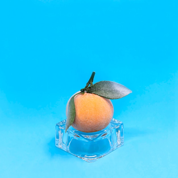 Mandarina congelada en cubitos de hielo sobre fondo azul.