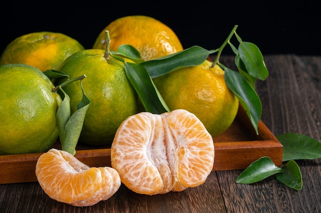 Mandarina mandarina verde fresca con hojas frescas en la mesa de madera oscura con fondo negro concepto de cosecha.