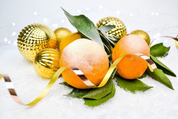 Mandarinas, bolas navideñas doradas en la nieve.