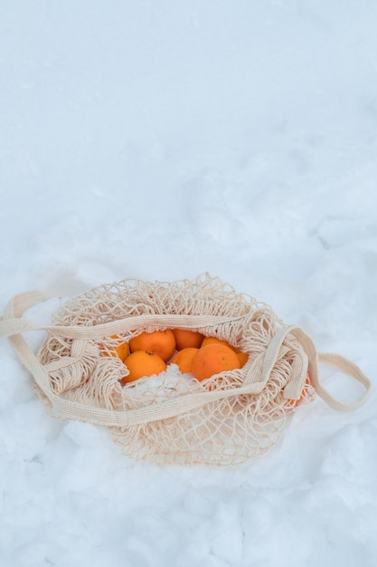 Mandarinas en una bolsa de hilo abierta yacen en la nieve Picnic en invierno en el bosque de invierno