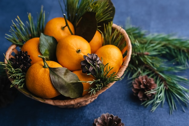 Mandarinas en una cesta de madera decorada con ramas de pino.