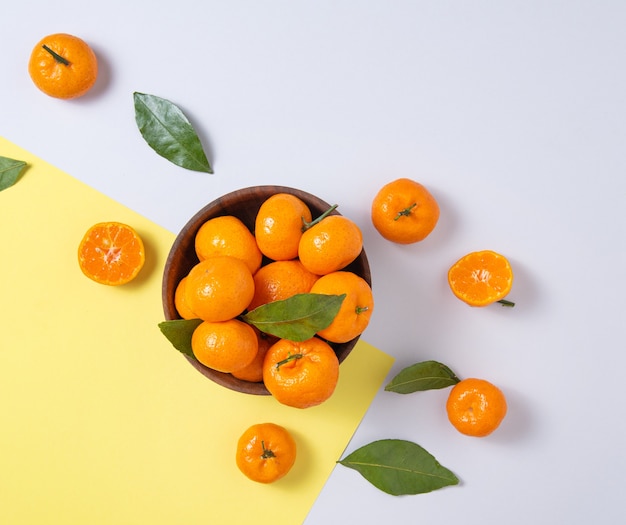 Mandarinas dulces y jugosas con hojas verdes en un cuenco de madera sobre un moderno fondo amarillo-gris. Vista superior y espacio de copia