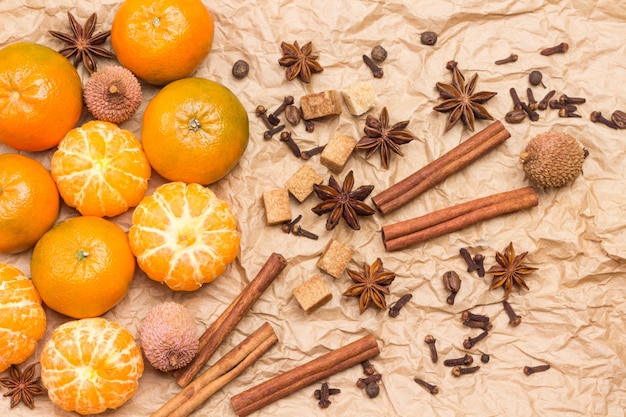 Mandarinas y especias enteras y peladas. Palitos de canela, anís estrellado, pimienta de Jamaica y cardamomo, lichi y nuez. Fondo de papel marrón. Endecha plana