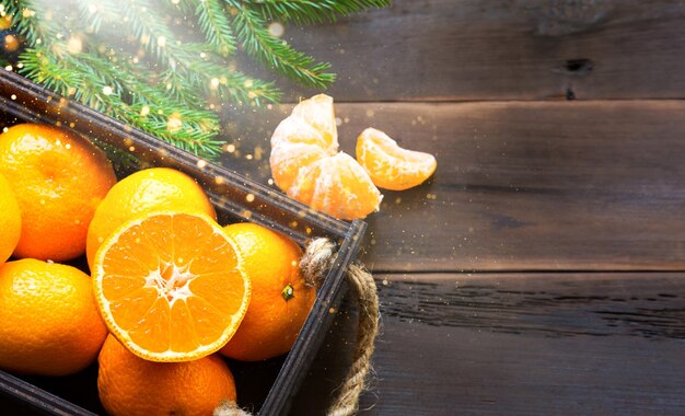 Foto mandarinas frescas en caja marrón sobre fondo de madera con ramas de abeto verde. marco, espacio de copia, fragancia de vacaciones e invierno, año nuevo, navidad. comida sana, zumo de naranja, escaparate. rebanar y cortar