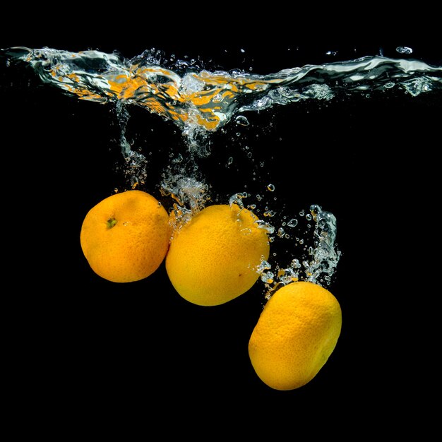 Mandarinas frescas cayeron al agua con burbujas en negro