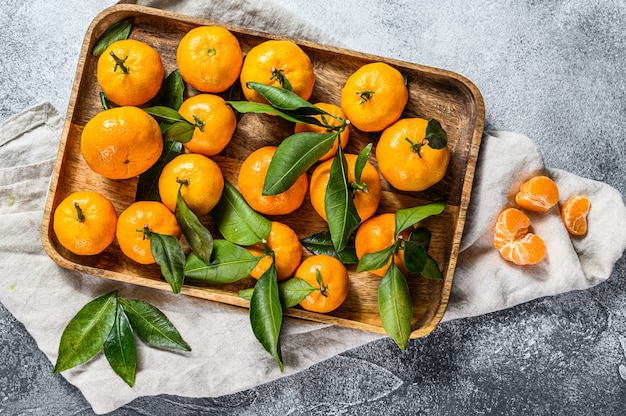 Mandarinas frescas frutas o mandarinas con hojas en un recipiente de madera. Vista superior