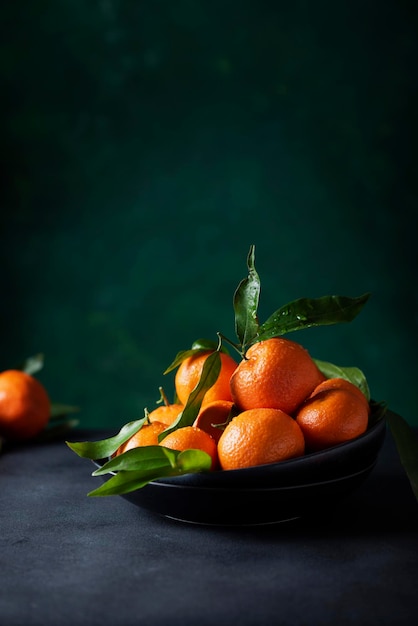 Foto mandarinas frescas con hojas verdes en el fondo oscuro, imagen de enfoque selectivo