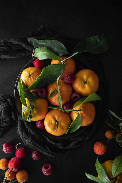 Mandarinas frescas y maduras con hojas verdes y frambuesas sobre un fondo oscuro