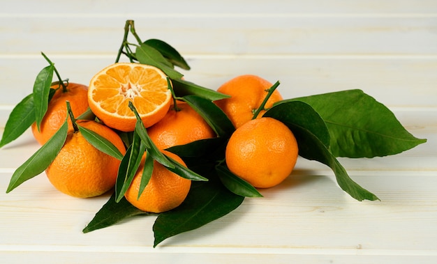 Mandarinas con hojas sobre la mesa de madera blanca.