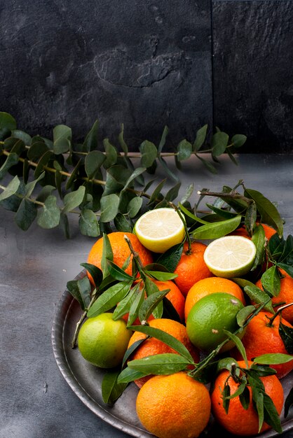 mandarinas con hojas verdes sobre una placa de metal, sobre un fondo gris