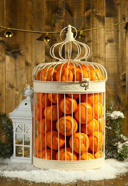 Mandarinas en jaula decorativa, sobre fondo de madera