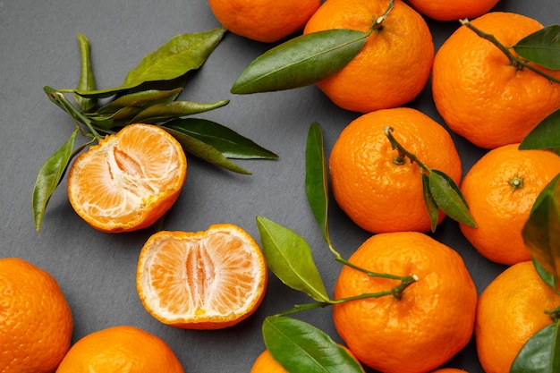 Mandarinas naranjas con hojas verdes sobre un fondo gris La mandarina se divide por la mitad en partes Vista superior