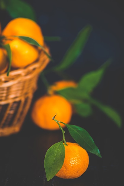 Mandarinas, naranjas, mandarinas, clementinas, frutas cítricas, con hojas en canasta sobre madera rústica oscura