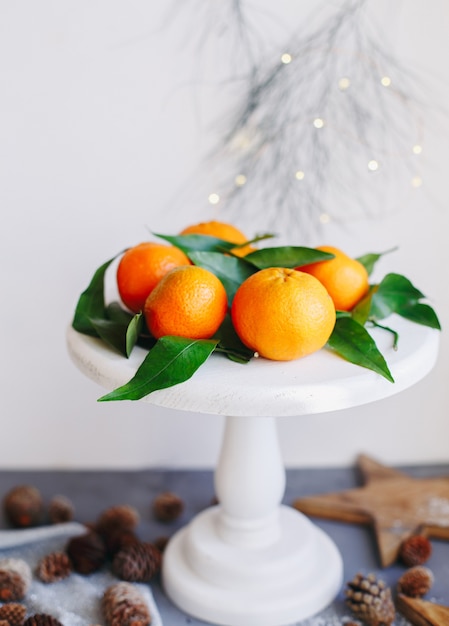 Foto mandarinas naranjas sobre fondo gris en la decoración de año nuevo con conos de pino marrón y hojas verdes. decoración navideña con mandarinas. clementina dulce deliciosa.