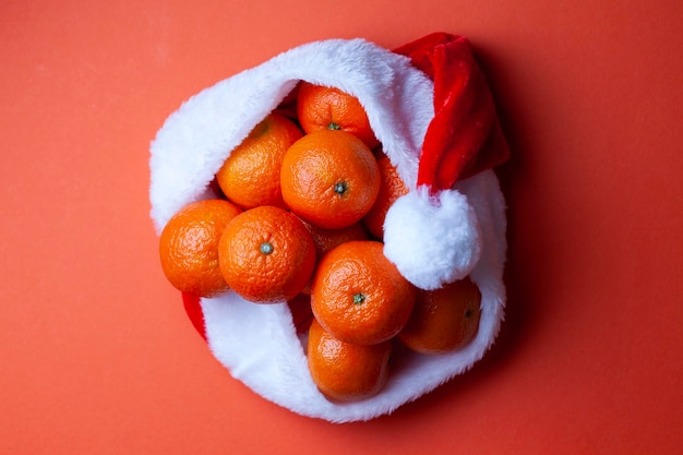 Mandarinas navideñas en un sombrero de Papá Noel sobre un fondo naranja Símbolo festivo de frutas navideñas