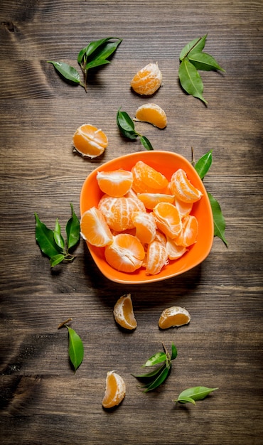 Mandarinas peladas en un recipiente con hojas sobre la mesa de madera. Vista superior